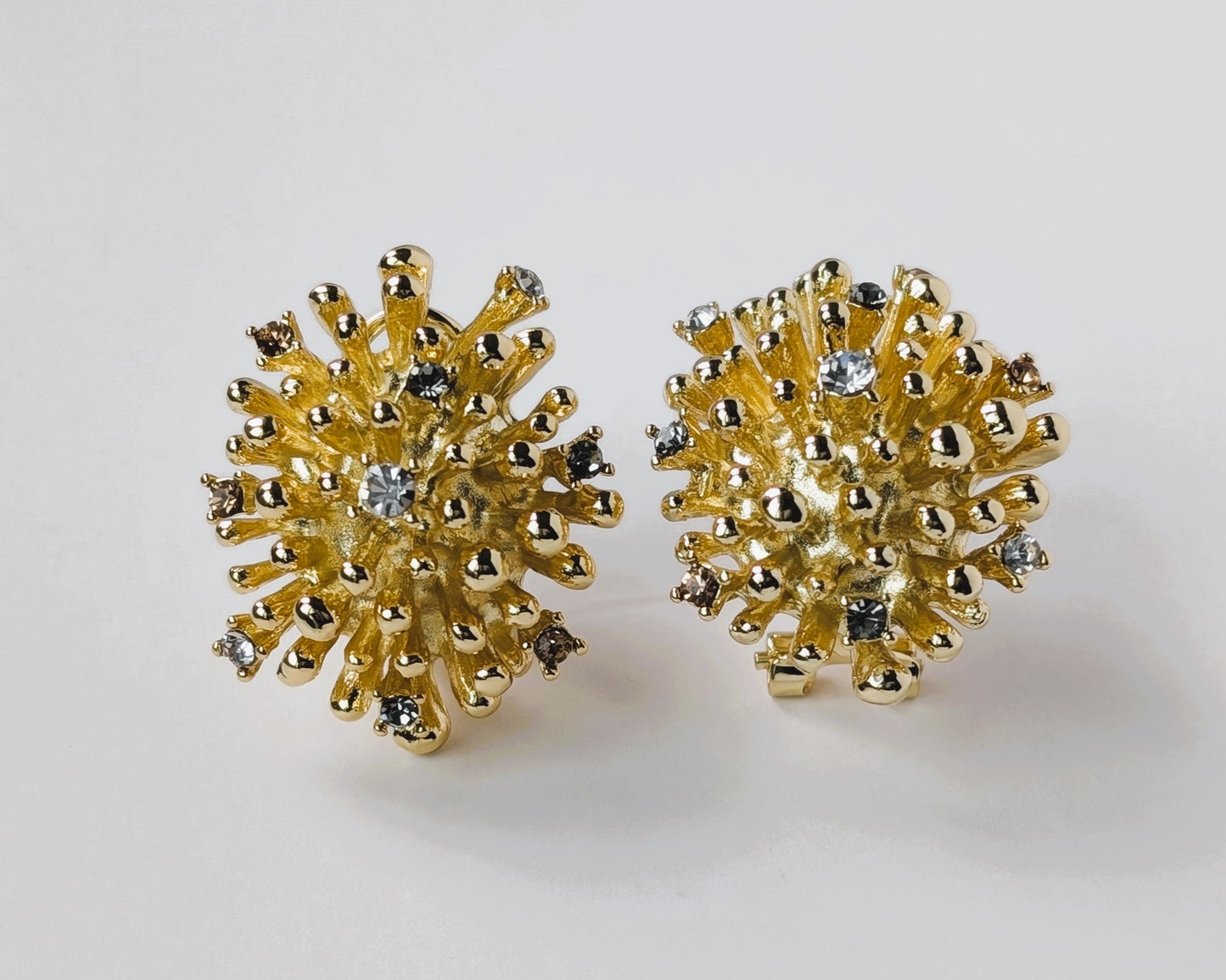 Gold floral earrings with gemstones on a light gray background