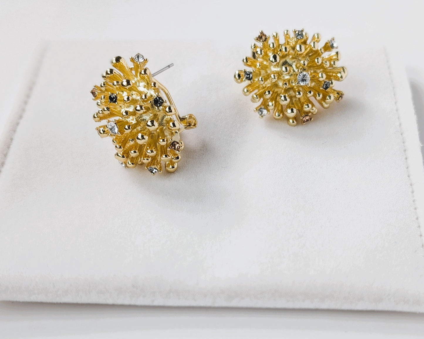 Gold earrings with gemstones on a white cloth background