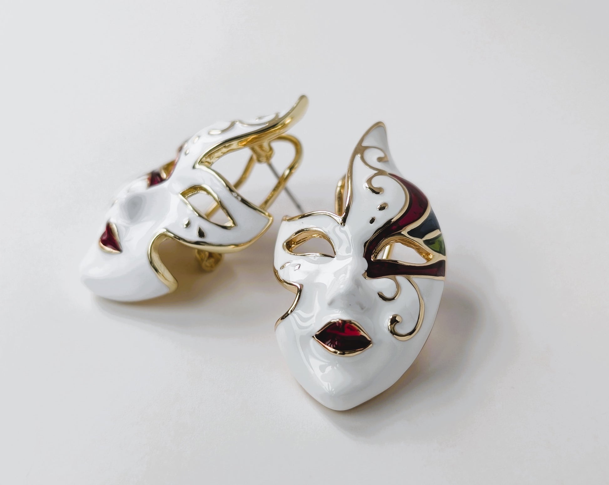 Pair of white mask earrings with gold accents on a light gray background